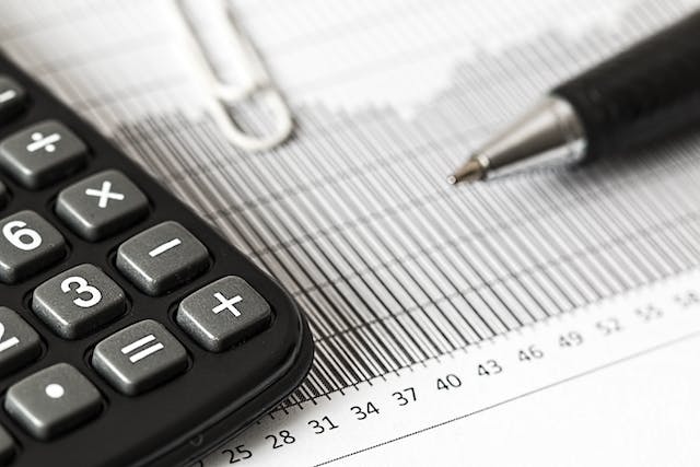 Nahaufnahme eines Taschenrechners, eines Stifts und einer Büroklammer auf einer Finanztabelle mit Zahlen und Balkendiagrammen, die die Auswirkungen der Grundsteuerreform veranschaulichen.