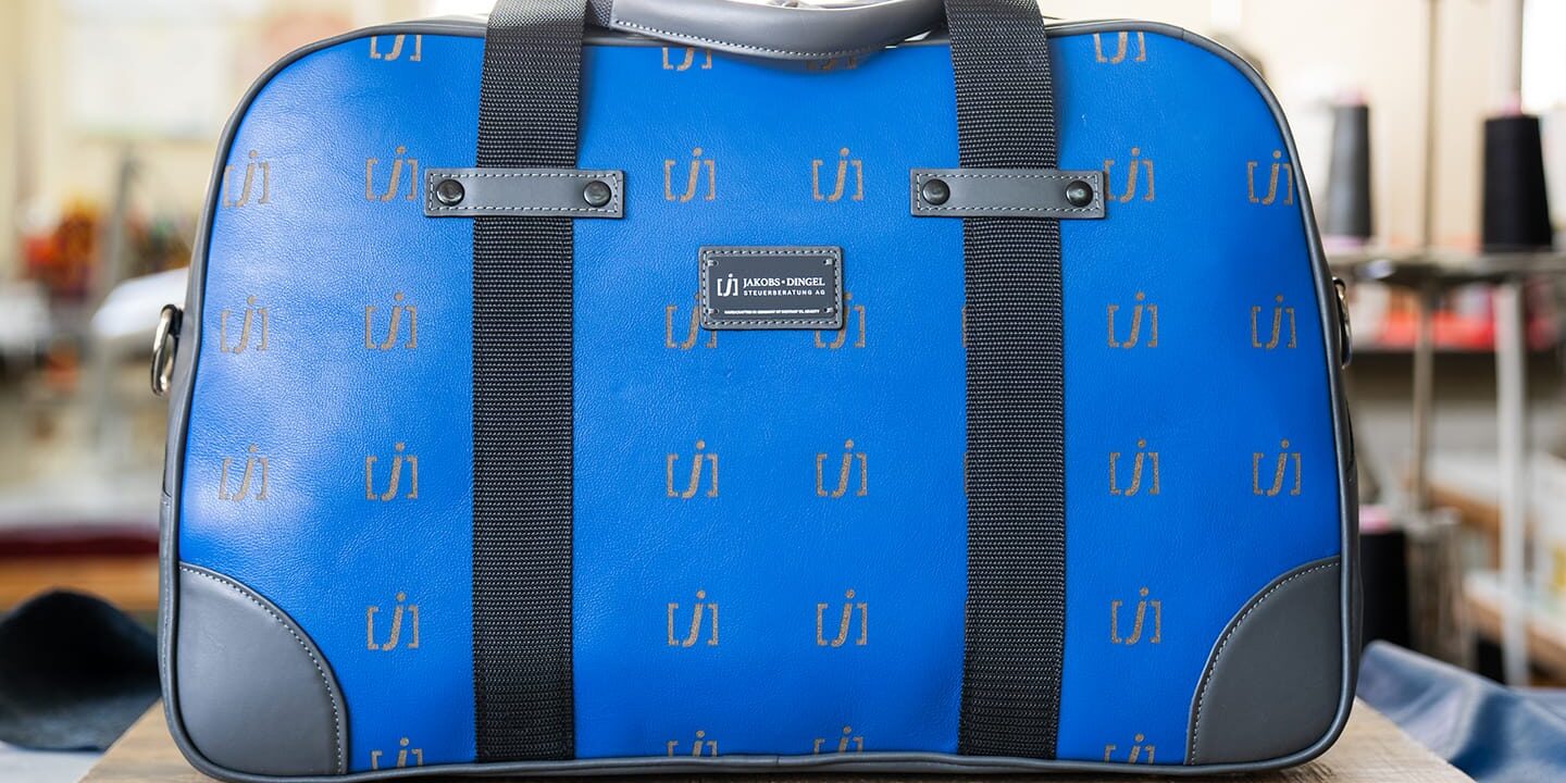 Ein blauer Seesack mit schwarzen Trägern und Eckakzenten liegt auf einer hölzernen Oberfläche in einem Innenraum, perfekt für die Präsentation in Ihrem nächsten Social-Media-Gewinnspiel-Post.