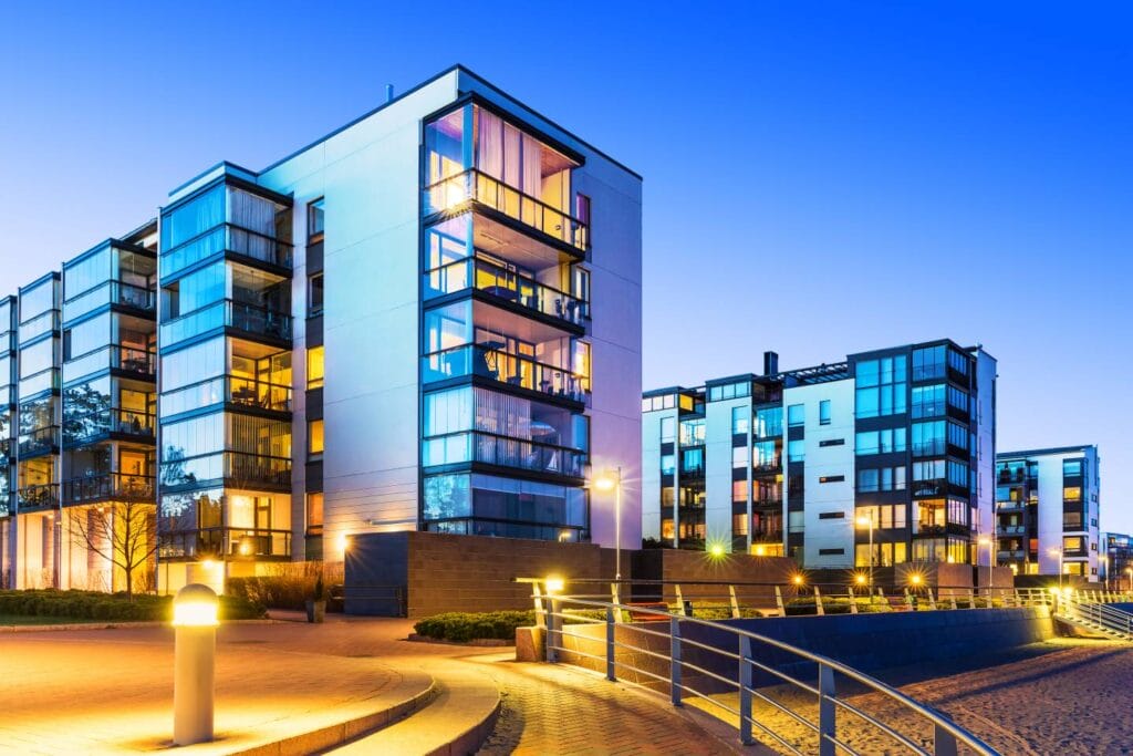 Moderne Mehrfamilienhäuser mit großen Fenstern, beleuchtet in der Dämmerung, neben einem Gehweg und Geländer - ein ideales Umfeld für Immobilien in Deutschland und smarte Finanzplanung.
