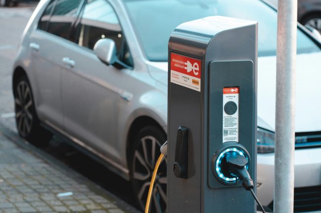 Silbernes Elektrofahrzeug an einer Ladestation in der Stadt, Blaulicht am Ladegerät - ein Zeichen für steuerliche Vorteile und moderne Mobilität.